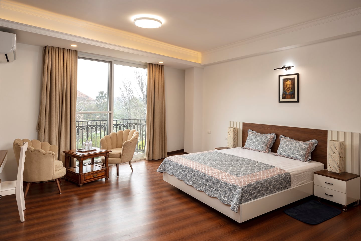 A light-filled room at Luminous, with a double bed, two armchairs beside the balcony doors and warm wooden floors.